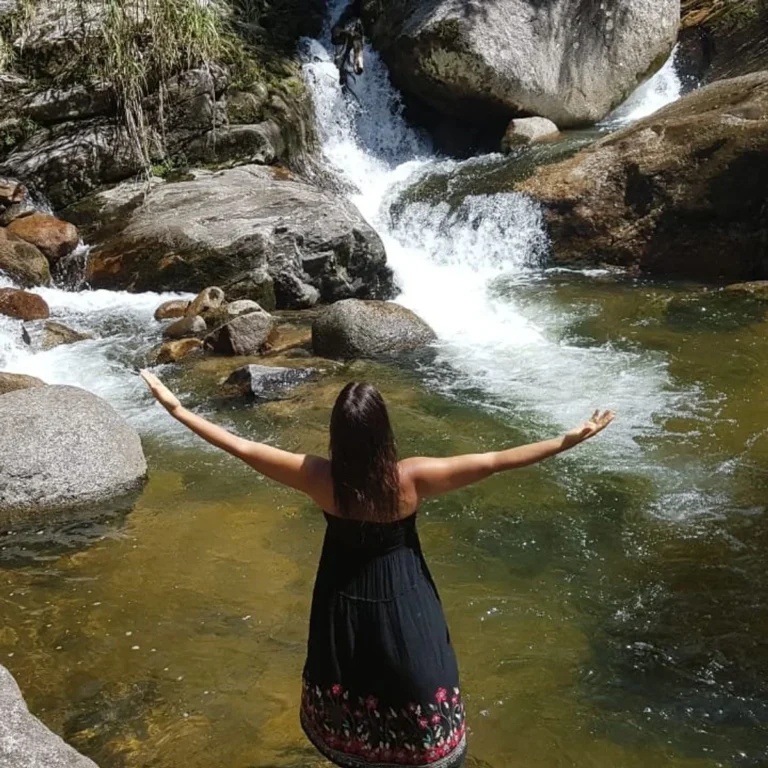 Mulher de braços abertos diante de cachoeira no Arraial do Sana