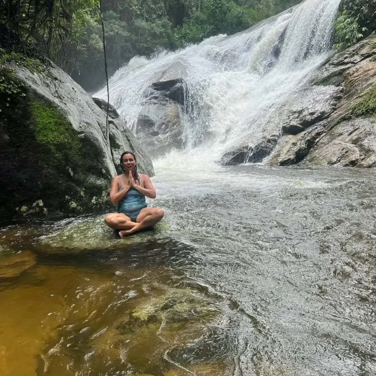 Mulher meditando sobre pedra diante de cachoeira no Sana